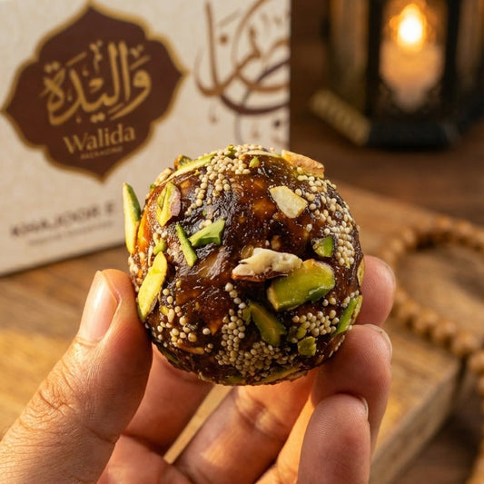 Hand holding a Khajoor Special Laddu with Roasted Nuts  Walida Special Khajoor Laddu box in the background
